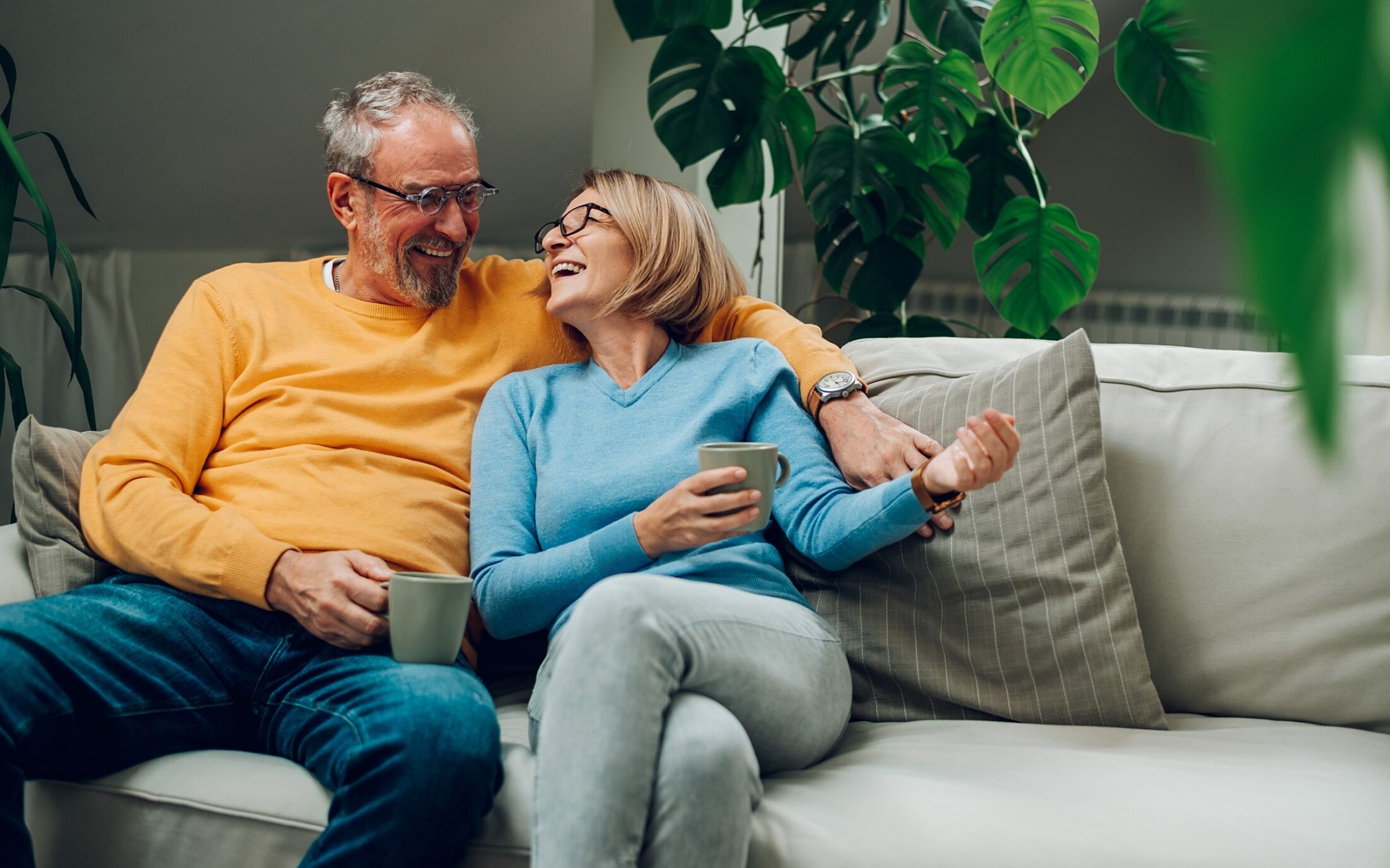 Portrait of a happy elderly couple hugging and relaxing together on the sofa at home and drinking coffee 2228197849